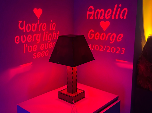 TPersonalised Message Projection Table Lamp on a stand with personalized text on a wall behind it